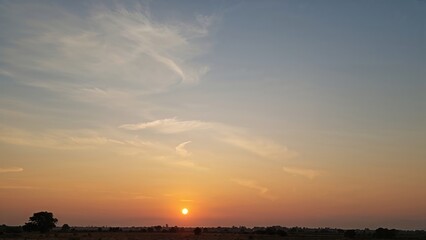 Sunset scene with a low sun on the horizon, clear sky with some clouds, and a flat landscape in the foreground.