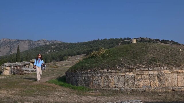 A woman walking beside monumental tumulus tombs in the Hierapolis Necropolis (Turkey), visiting the open-air museum.