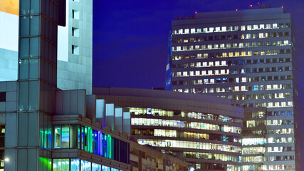 Modern office building in city center illuminated at night. Rows of lit windows against the architectural grid of a modern facade.
