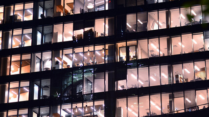 Modern office building in city center illuminated at night. Rows of lit windows against the architectural grid of a modern facade.