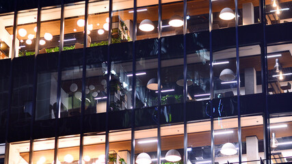Modern office building in city center illuminated at night. Rows of lit windows against the architectural grid of a modern facade.