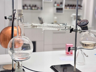 laboratory setup with glass round bottom flask connected to a condenser coil on a white counter concept of chemistry, distillation, scientific research