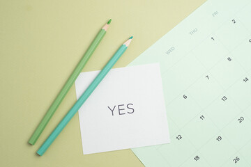 The word 'YES' on a calendar with pencils for planning and commitment. Affirmative decision
