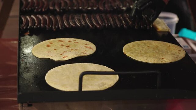 Dark blood sausages and flatbreads sizzle on a hot griddle. This scene evokes the authentic atmosphere of street food, perfect for culinary blogs, travel guides, or market promotions.