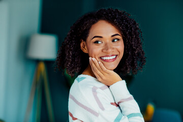 Smiling woman with curly hair in a cozy living room enjoying a calm home day interior lifestyle...