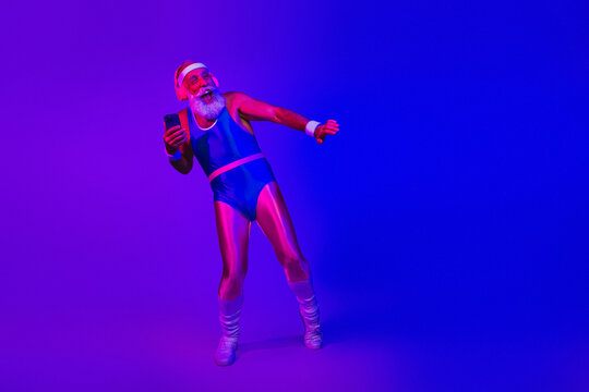 Energetic senior man in retro athletic suit dances and photographs while using a smartphone under vibrant purple and blue neon lights - Powered by Adobe