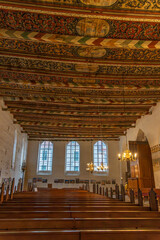 Nave of the historic Church of the Holy Spirit, featuring a uniquely and artistically painted wooden ceiling, with a view forward of bright windows and the organ.