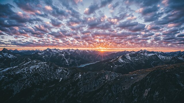 Sunset over the mountain range during dusk with clouds and snow-capped peaks. Landscape and nature scene. The view of mountains and sky during sunset. - Powered by Adobe