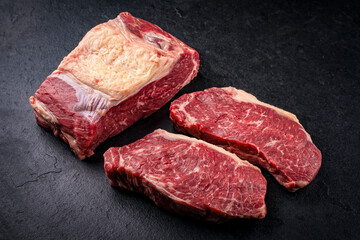 Raw dry aged  roast beef steak offered as close-up on a design slate plate