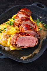 Pork fillet roast wrapped in prosciutto ham bacon with polenta and fresh herbs in serving cast iron skillet