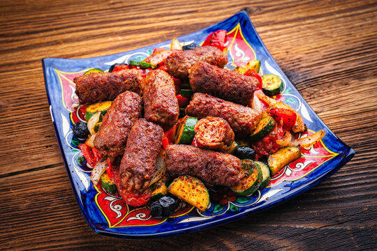 Traditional Croatian cevapi spicy meat ball rolls with troasted vegetables served as close-up on a rustic plate