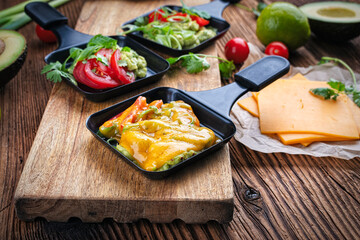 Vegetarian raclette with mached avocado, lime and cheddar cheese served as close-up on a wooden design board