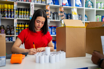Young woman working in an auto parts store, writing on paperwork at the counter