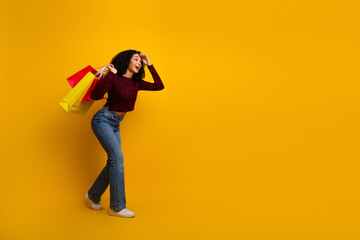 Young mixed race woman with shopping bags smiles and walks against a bright yellow background in casual stylish outfit