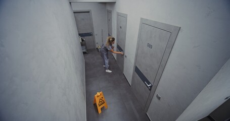 Hotel Cleaning Staff in Neat Uniform Thoroughly Cleans Door Frame, Handle and Metal Lock With Gentle Cloth and Disinfectant. Concept High Standard Housekeeping, Cleanliness and Care. High Angle.