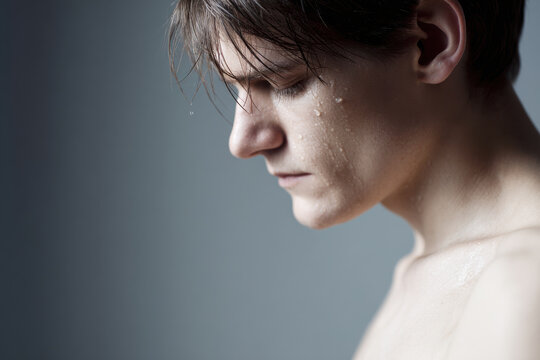 young man with wet eyelashes and heavy breath stands against clean solid background