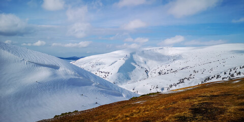 Panoramic view of snowy mountain slopes and deep valley under clear blue sky in bright sunlight. Peaceful winter nature background.