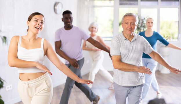 Portrait of cheerful young girl enjoying active dancing during group training with adults people of different ages in dance studio