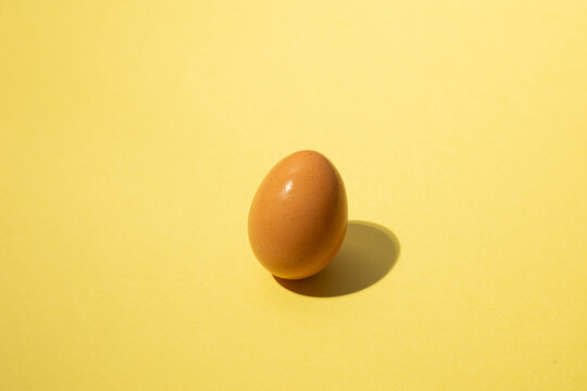 Brown egg standing upright on a yellow background.