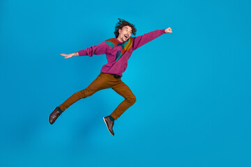 Fototapeta premium Joyful young man leaps in a colorful sweater against a bright blue background