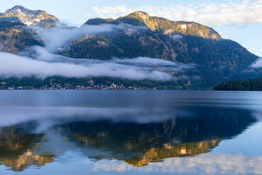 Ein stiller See spiegelt majest&auml;tische Berge im Morgenlicht. Nebelschwaden ziehen &uuml;ber das Wasser und verleihen der friedlichen Landschaft eine mystische Atmosph&auml;re.