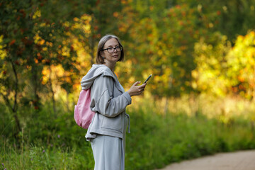 Young woman exploring nature with a smartphone in a vibrant park during autumn