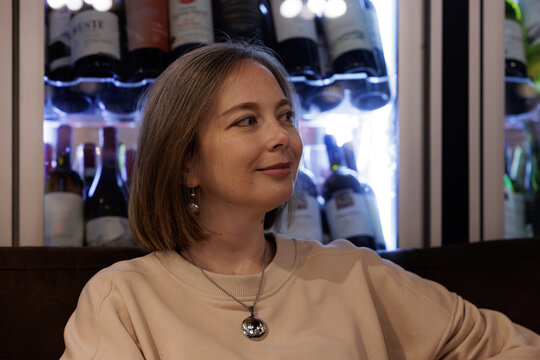 Smiling woman enjoying a relaxing moment in a cozy wine cellar surrounded by bottles in the evening