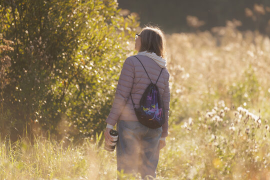 Woman enjoying a peaceful stroll through a sunlit field surrounded by nature's beauty in autumn