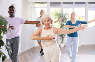 Dynamic mature attendees of dancing courses training poses of Waltz in dance hall