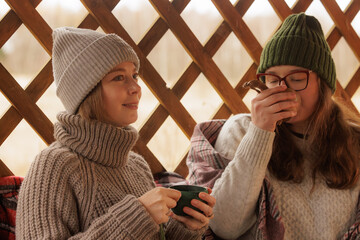 Friends enjoying warm drinks together in a cozy outdoor cabin during a chilly afternoon