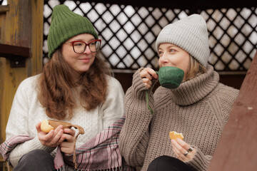 Friends enjoy warm coffee and snacks in cozy sweaters while relaxing in a rustic wooden gazebo