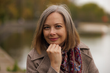 Woman poses thoughtfully by a serene lake, surrounded by autumn foliage in a peaceful, reflective moment