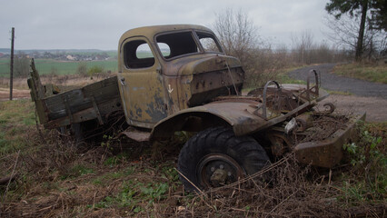 Fototapeta premium rusty truck with missing parts and weeds, deteriorated pickup surrounded by nature and neglected elements