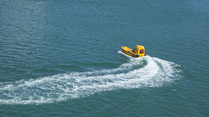Bright yellow motorboat gliding across calm blue waters, leaving a white wake behind, showcasing a serene maritime scene and adventure spirit
