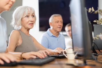 Portrait of an elderly positive woman working on computer with group of friends while attending PC classes in a nursing home