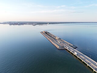 Aerial View Of Long Monitor Merrimac Memorial Bridge Tunnel crossing tranquil blue water of Hampton Roads Channel with a distant harbor and open sky
