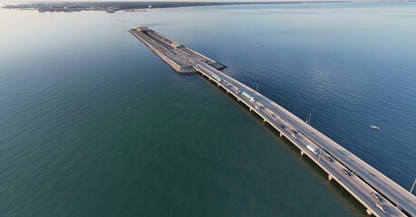 Aerial View Of Long Monitor Merrimac Memorial Bridge Tunnel crossing tranquil blue water of Hampton Roads Channel with a distant harbor and open sky