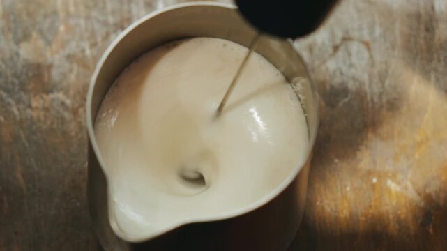 milk pitcher steamed creating creamy vortex under steam wand, barista aerates milk while coffee artist