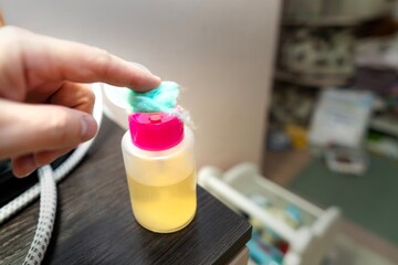 Man's finger pressing green cotton ball against vertical disinfectant dispenser for application