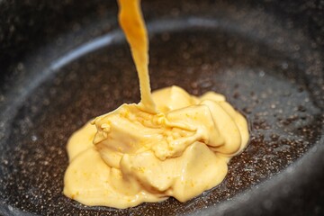Shiny honey batter with cream and butter being poured into non-stick pan for homemade cake.