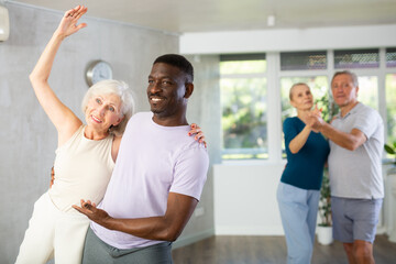 Happy smiling elderly woman enjoying impassioned merengue with african american partner in latin dance class. Social dancing concep