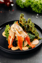 Smoked salmon salad with poached egg, hollandaise and spinach waffles on black plate