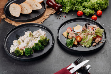 Two plated dishes: creamy chicken with broccoli and tuna salad with egg on dark table