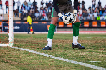 a soccer player goalkeeper in defense preparing to kick a football during a match, spectators on the stadium
