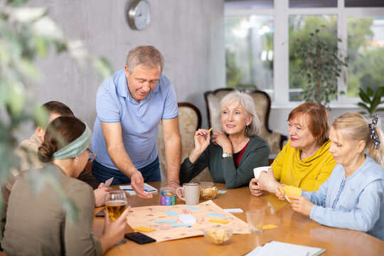 Portrait of happy elderly man playing interesting board game with friends at home. Seniors communication concept