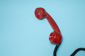 A bright red vintage telephone handset resting on a light blue background, creating a bold and...