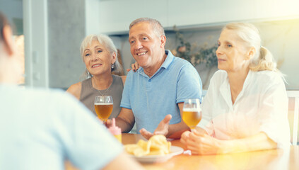 Happy elderly people speaking to each other with enthusiasm while drinking and eating in the kitchen