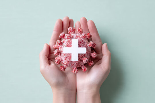 Hands holding small paper cutout of virus with white medical cross symbol, representing health protection and care during pandemic or virus outbreak