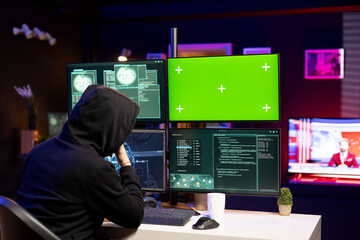 Cybercriminal coding on green screen PC, creating stealth malware that evades security. Hacker using chroma key computer to make script hiding malicious code from detection systems