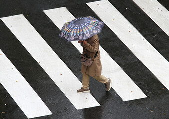 Persona con paraguas bajo el agua de la lluvia cruzando un paso de peatones